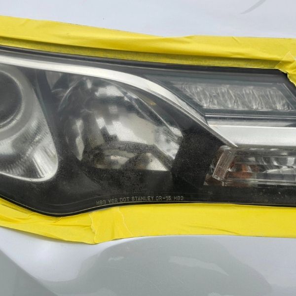 A car headlight partially covered in yellow painter's tape, likely in preparation for sanding or polishing.