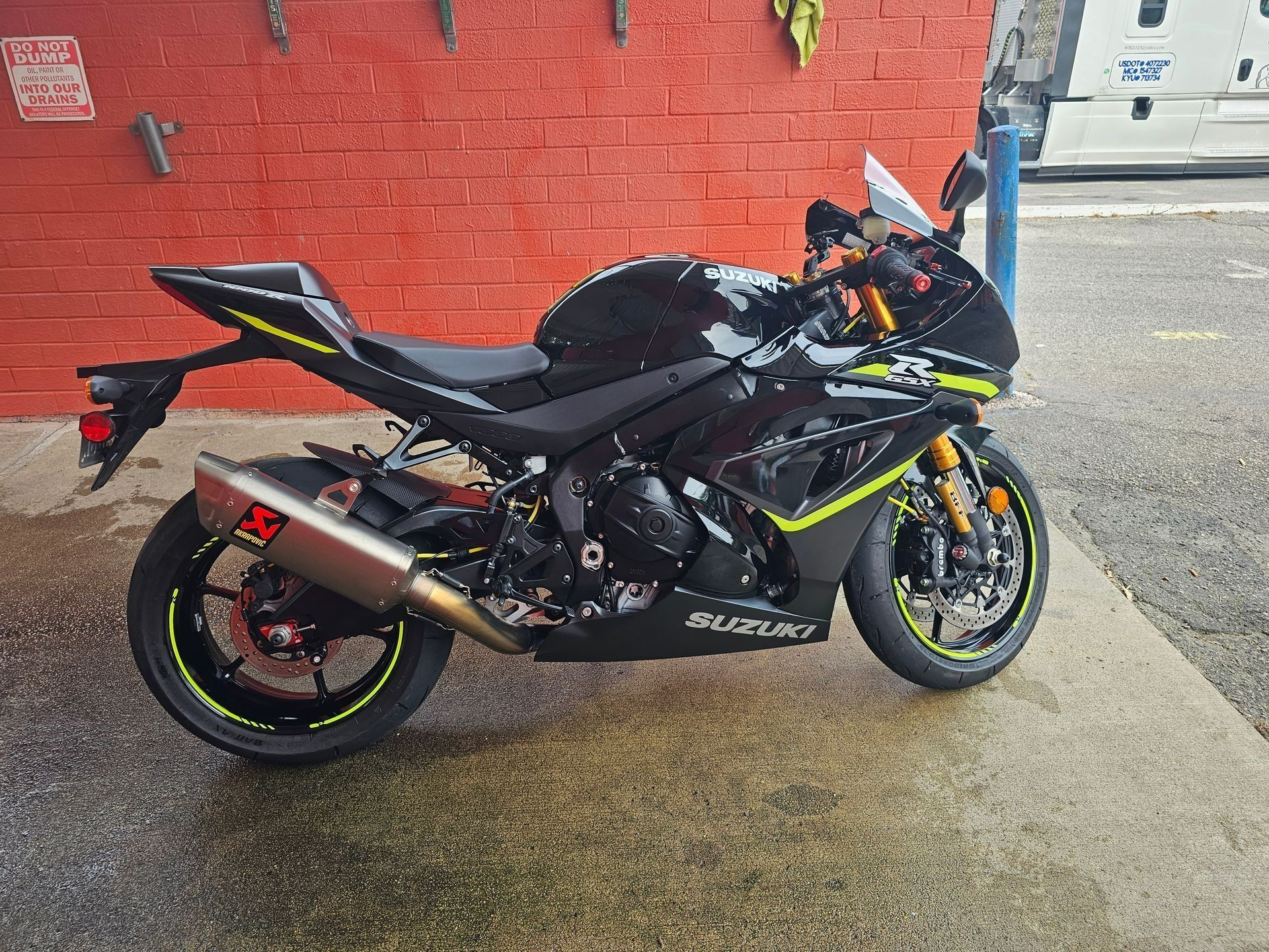 A black and yellow Suzuki sport bike parked on a wet concrete surface in front of a red brick wall.