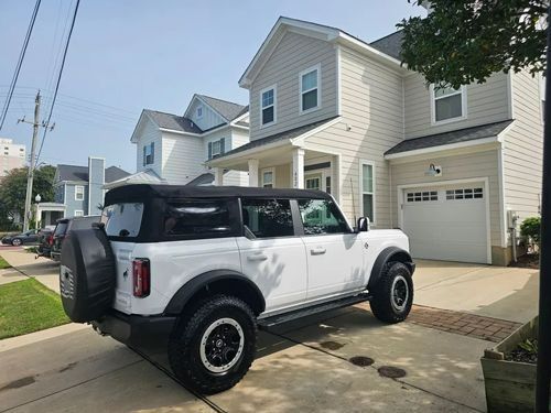 A white Ford Bronco parked in the driveway of a two-story suburban house on a sunny day.
