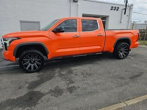 A bright orange pickup truck parked on an asphalt lot in front of a white building with the number 232 on the wall.