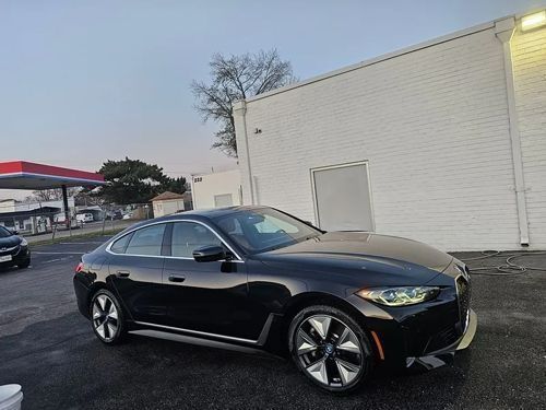 A black BMW sedan parked in an asphalt lot next to a white building, with a gas station canopy visible in the background.