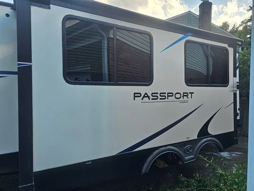 A cream-colored Keystone Passport travel trailer exterior with dark tinted windows, parked outdoors.