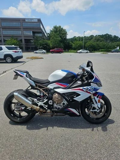 A BMW S1000RR sportbike with a white, blue, and red paint scheme parked in a sunny parking lot.