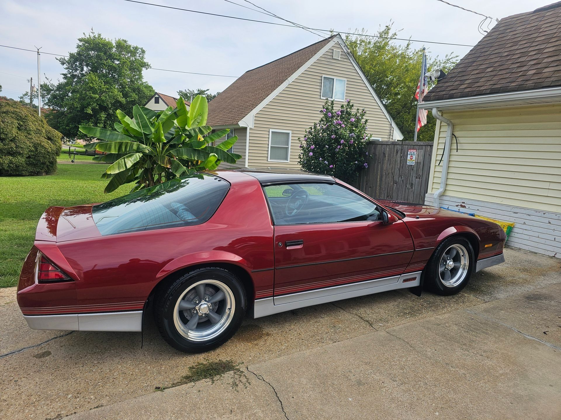 A dark red Chevrolet Camaro parked on a driveway next to a house with light-colored siding.