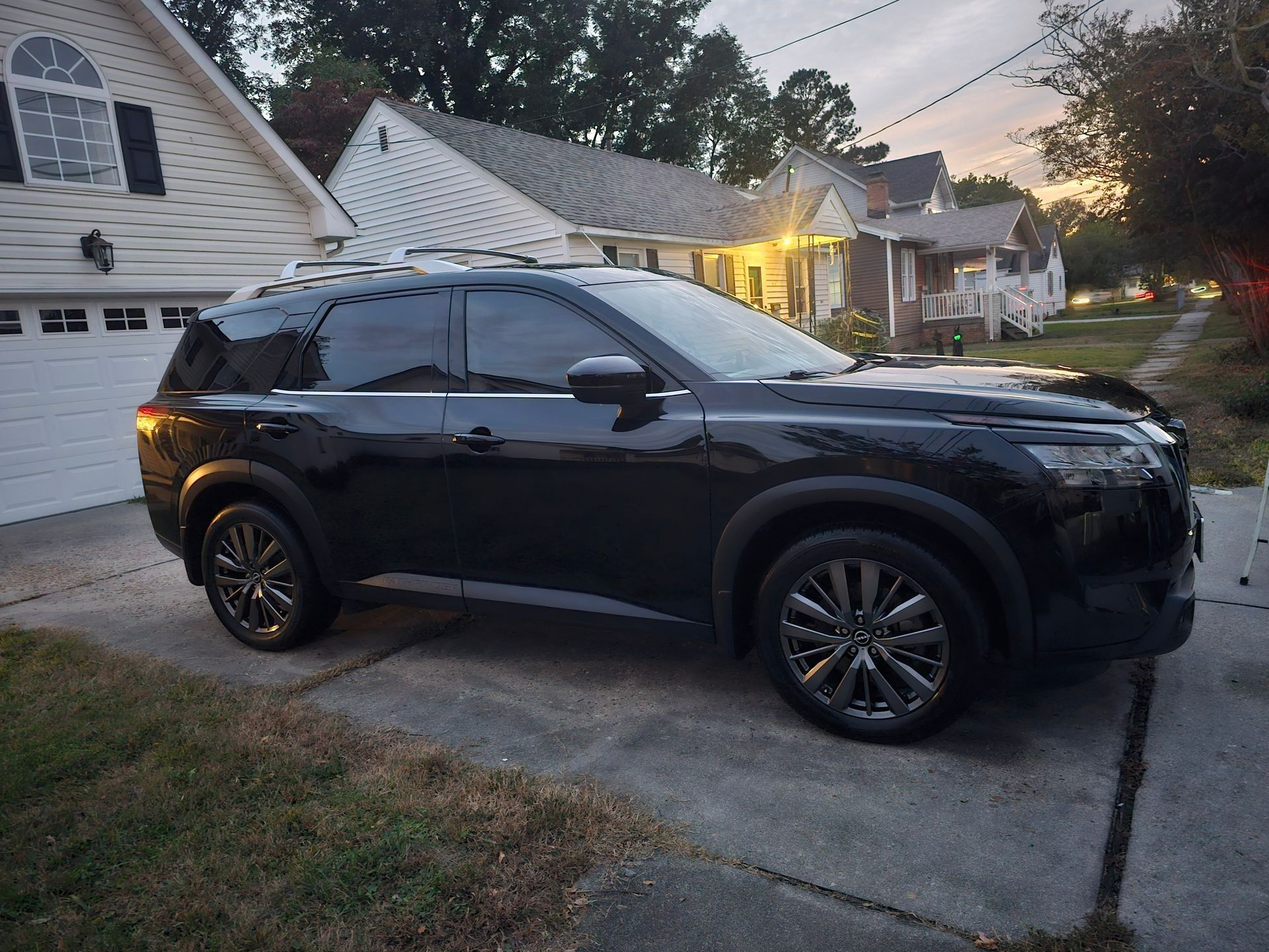 A black SUV parked on a residential driveway at dusk with a white house in the background.