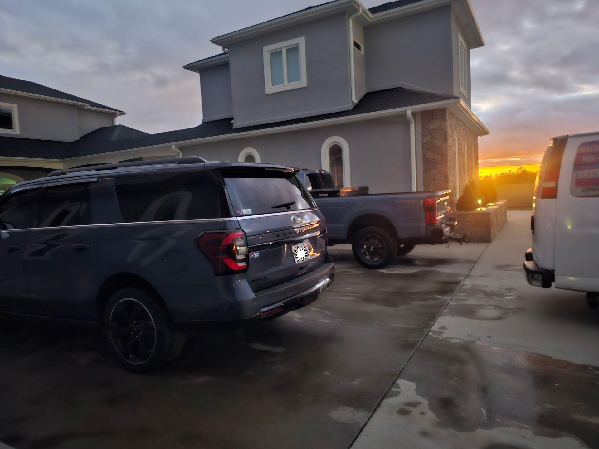 A grey SUV and pickup truck parked in a driveway in front of a house at sunset.