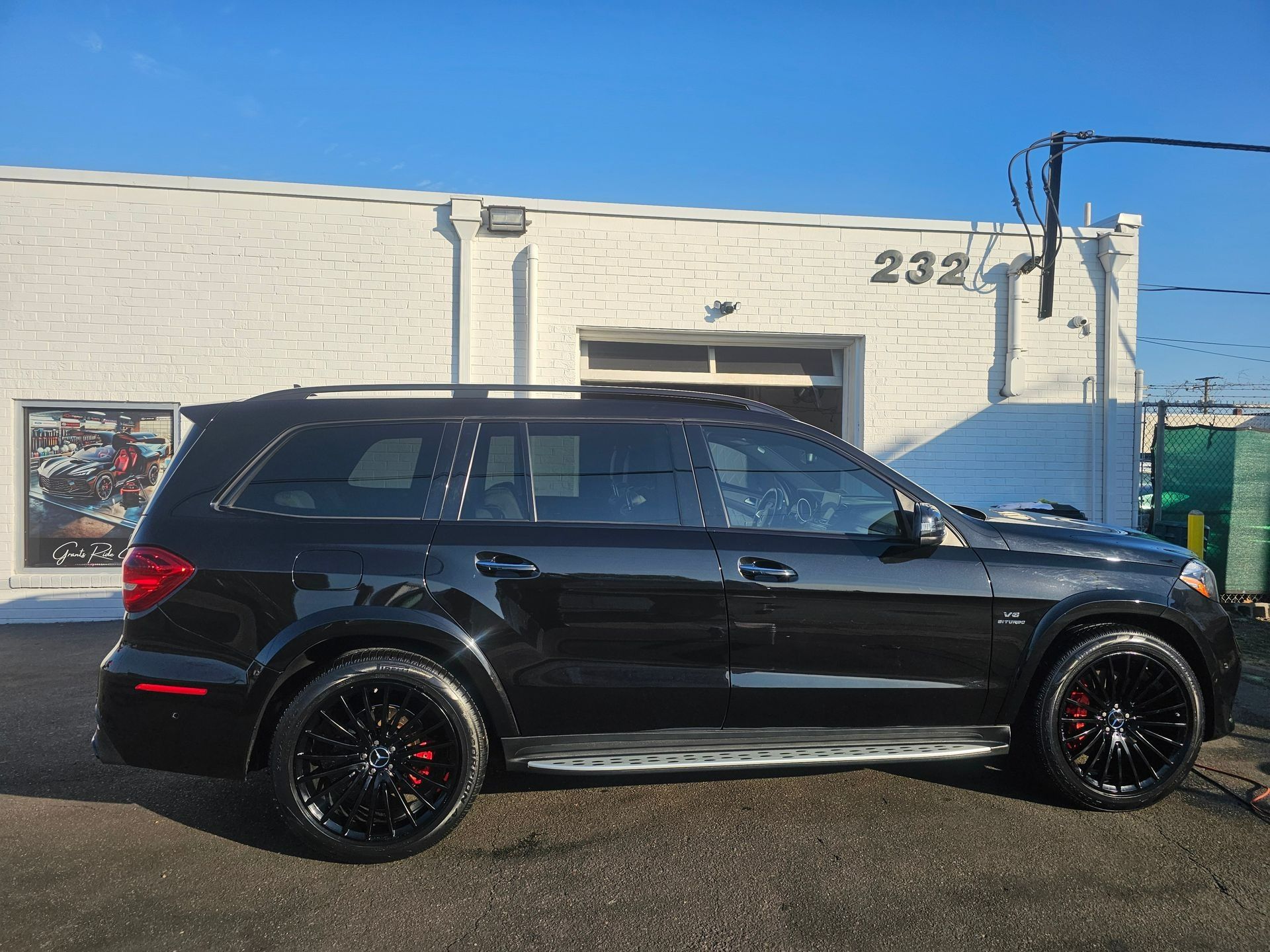 A black Mercedes-Benz SUV parked outside a white brick building labeled with the number 232.