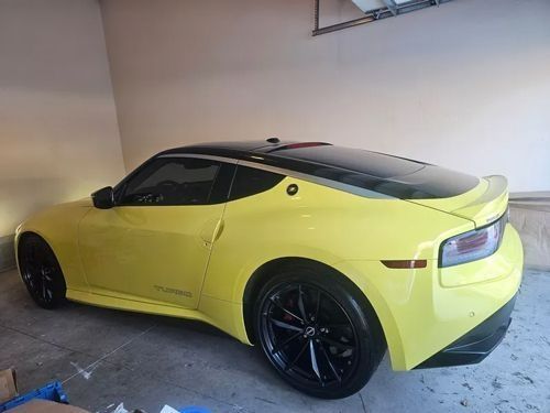 A bright yellow Nissan Z sports car with a black roof and wheels parked inside a garage.