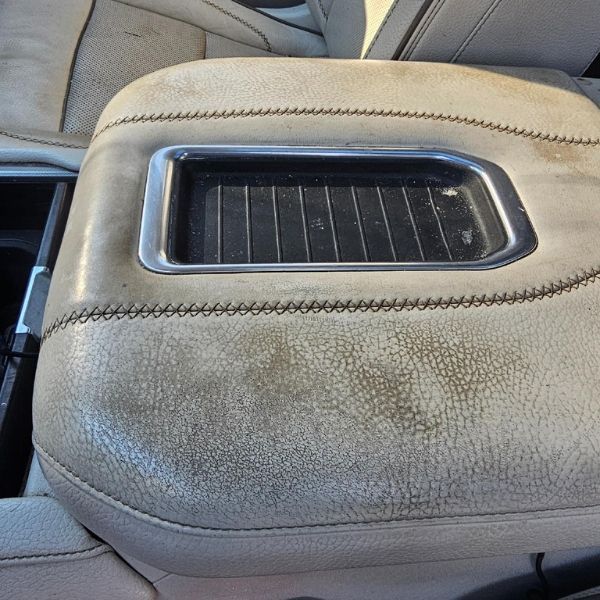 A worn, light-colored leather car center console with a black wireless charging pad in the center.