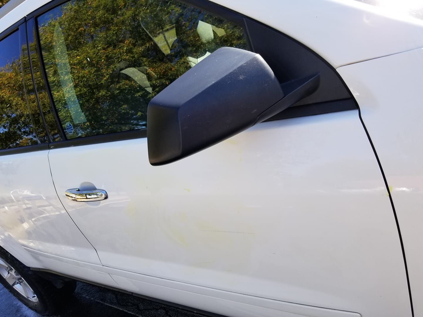 A white car door with a black side-view mirror, chrome handle, and visible body panel scratches.