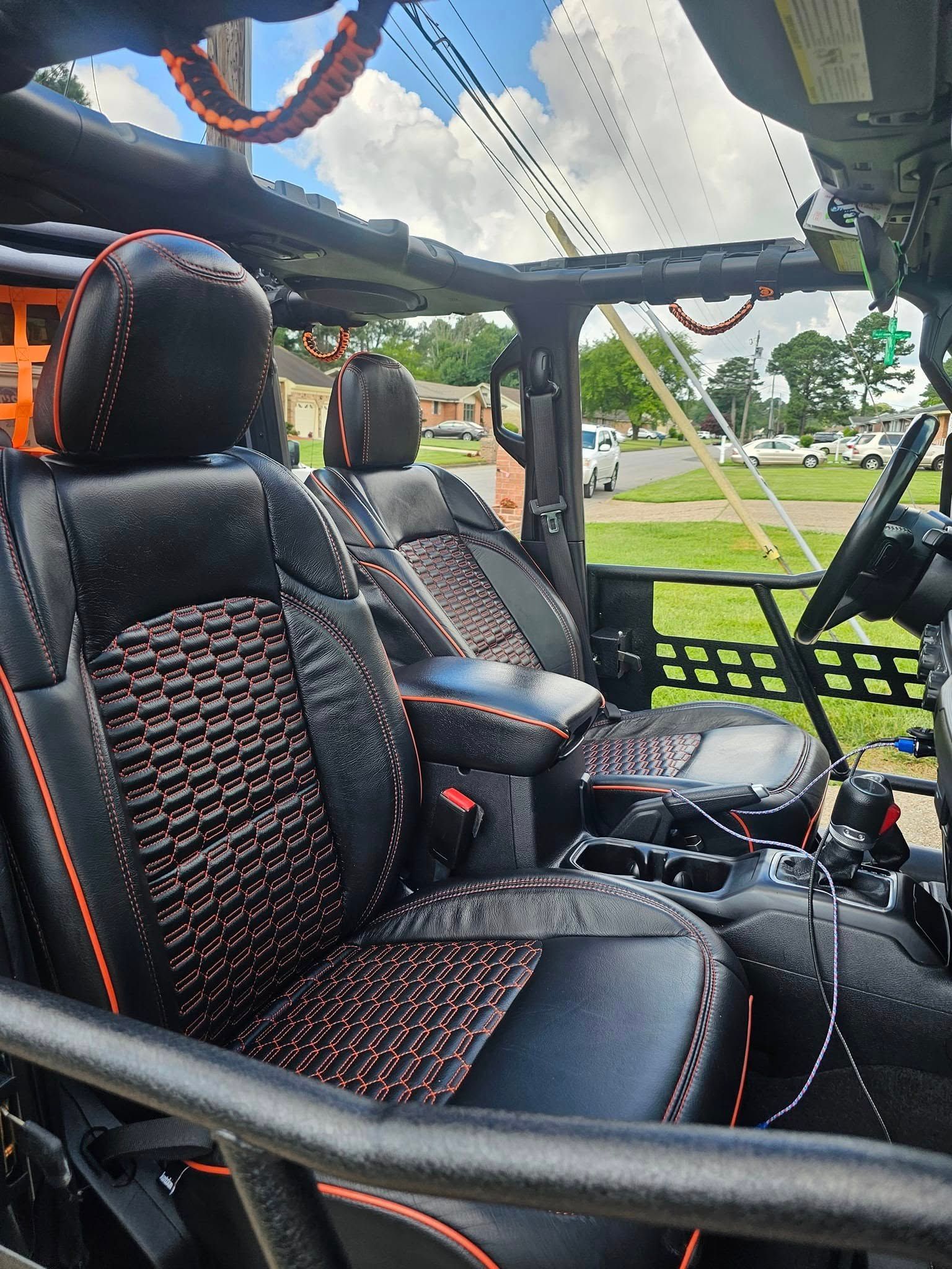 Interior view of a Jeep with black custom leather seats featuring orange patterned inserts and orange stitching.