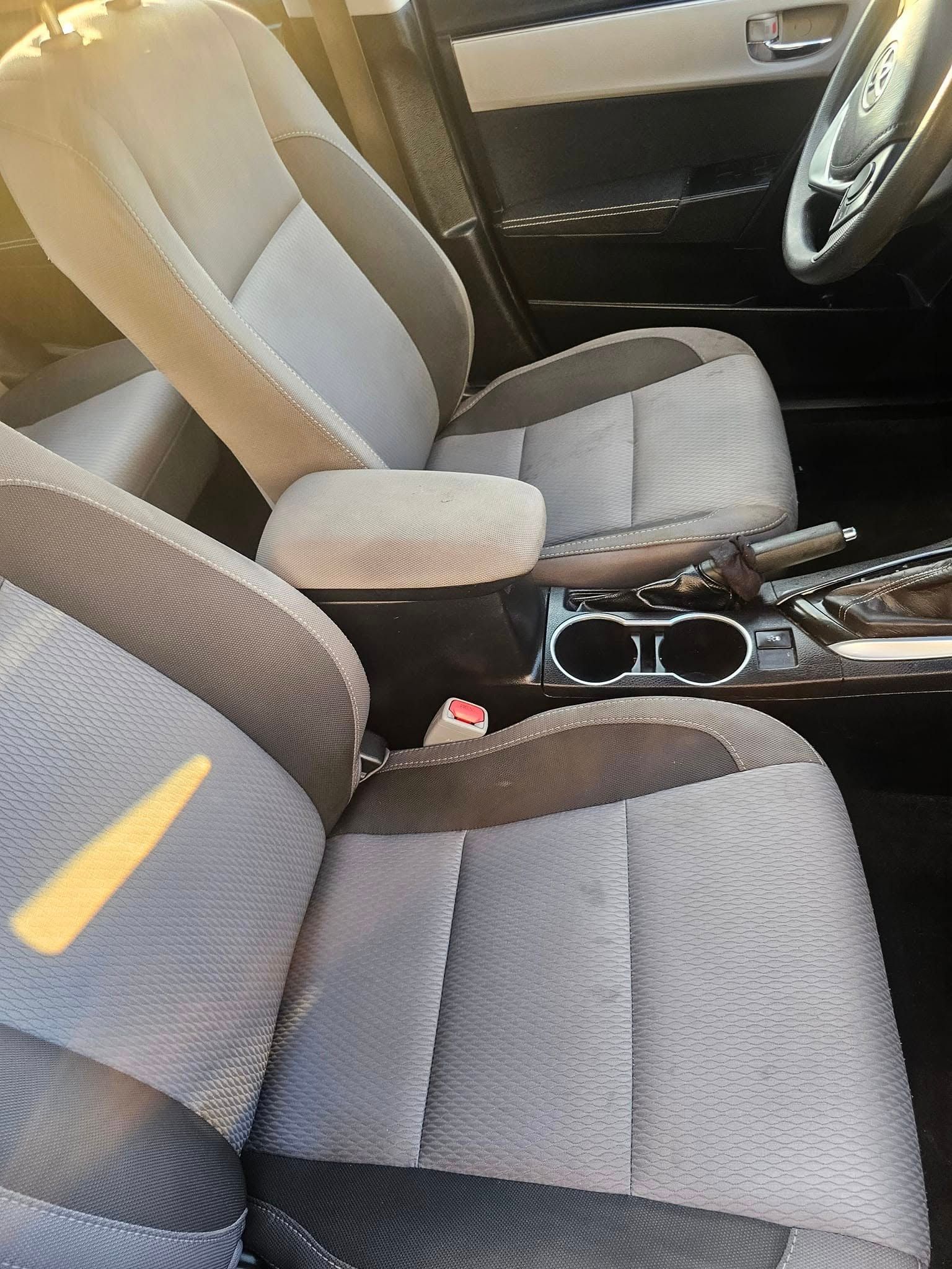 Interior view of a vehicle front cabin with grey patterned upholstery seats, a center console, and cup holders.