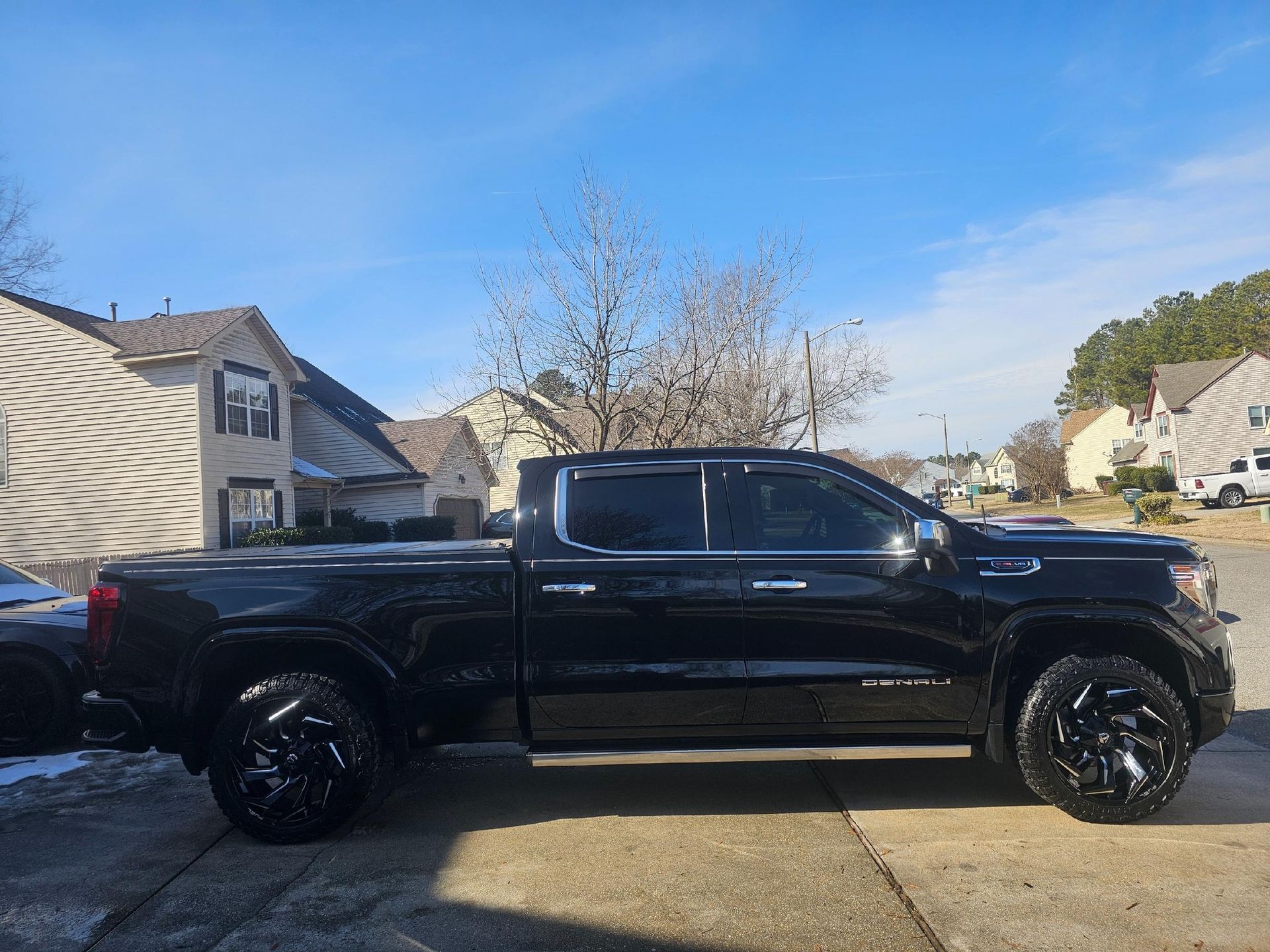 A black pickup truck with custom wheels parked in a residential driveway on a sunny day.