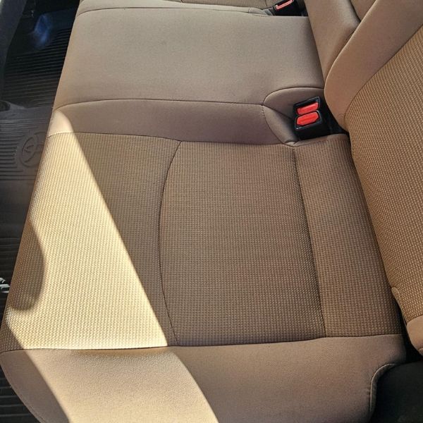 A close-up view of tan fabric vehicle seats with a visible seat belt buckle in a bright, sunlit interior.