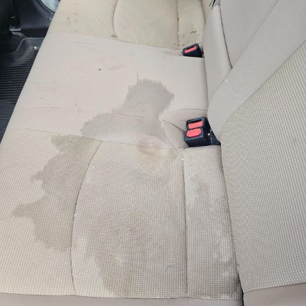 A large, wet spill stain on light-colored fabric car upholstery.