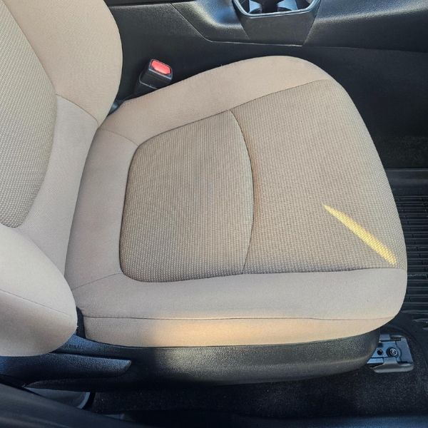 A beige upholstered car seat with a diagonal, yellow-colored stain on the cushion.