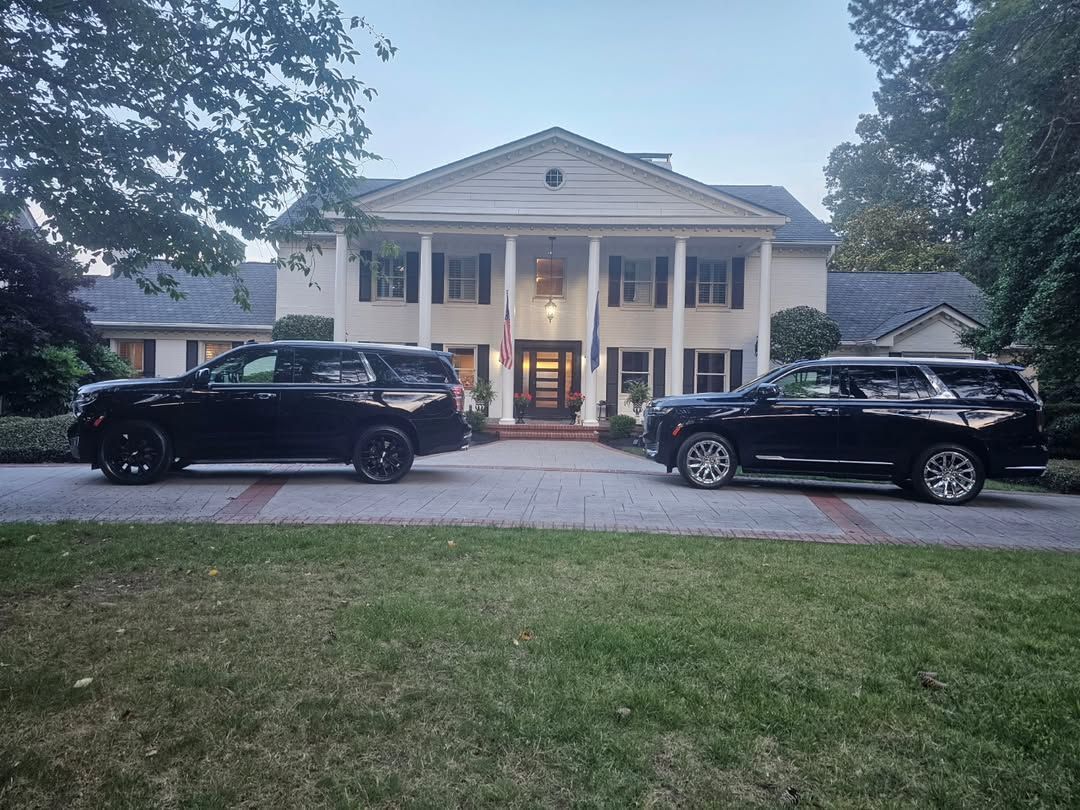Two black SUVs parked in front of a white, columned two-story colonial-style mansion at dusk.
