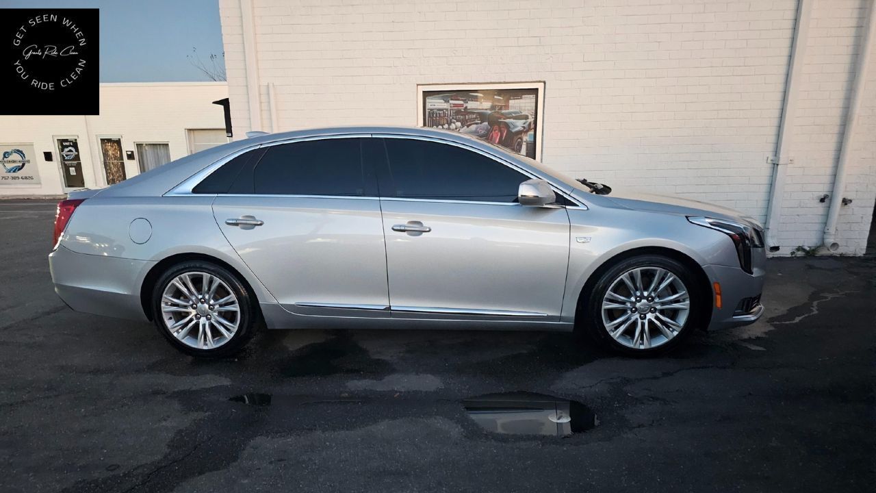 A silver Cadillac CT6 sedan parked in a parking lot next to a white brick building.