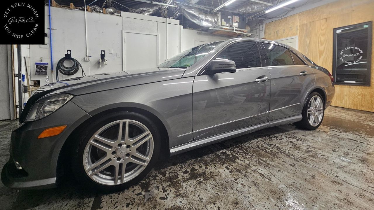 A grey Mercedes-Benz sedan parked inside a workshop with a concrete floor and plywood walls.