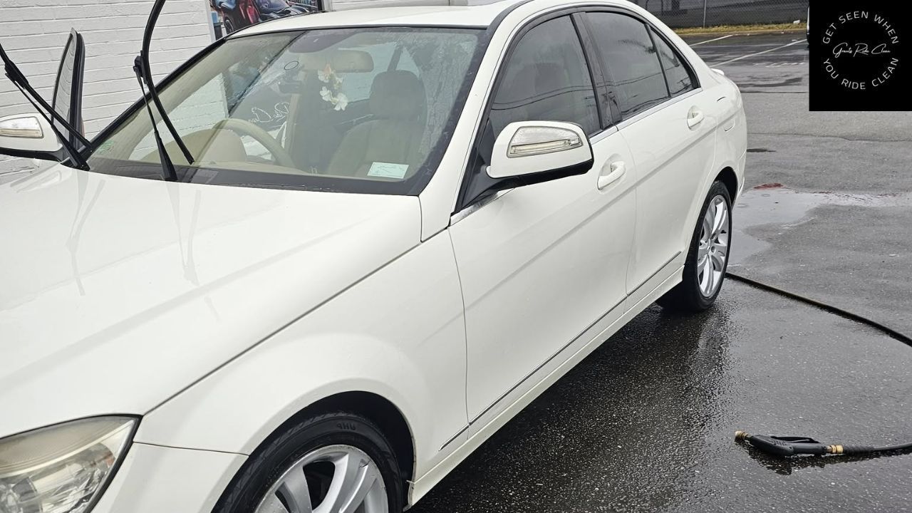 A white sedan parked on a wet surface with its windshield wipers raised.
