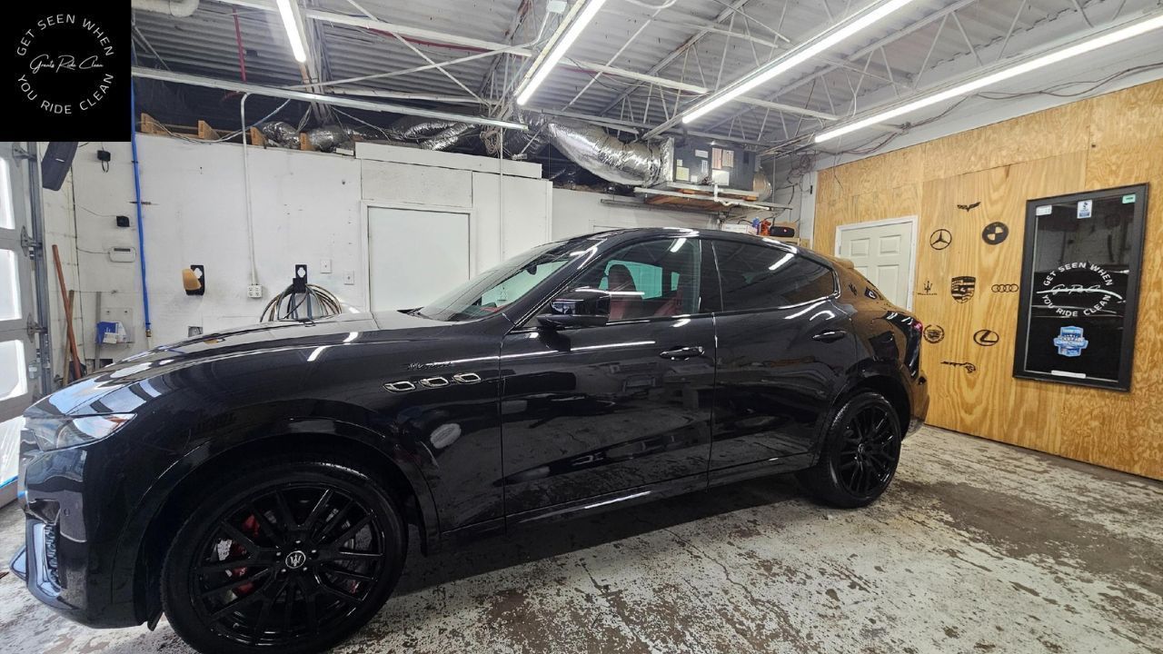 A shiny black luxury SUV parked inside an industrial-style workshop with white walls and a wood-paneled wall.