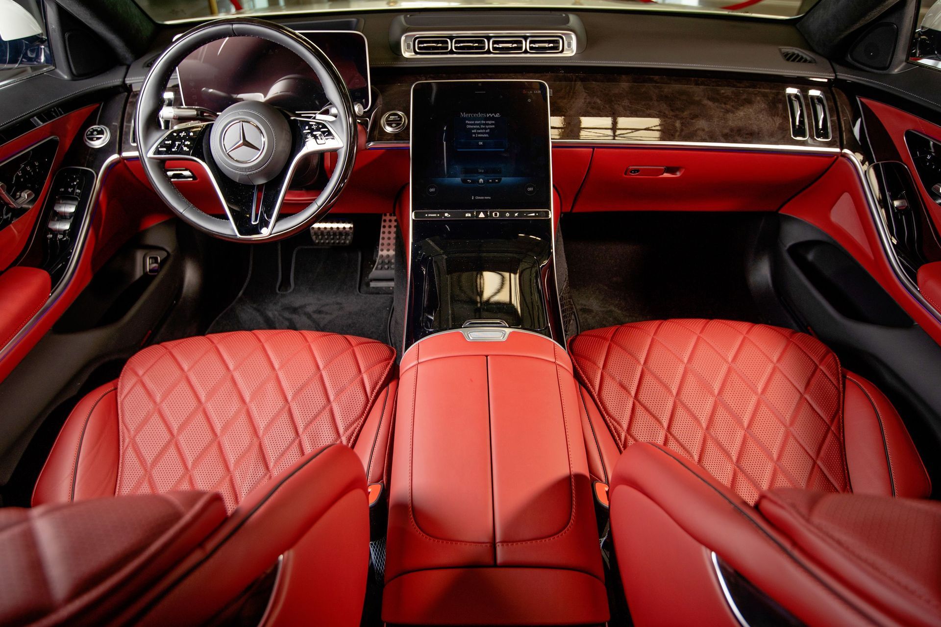 Luxury car interior with red leather seats, wood trim, and a large touchscreen dashboard.