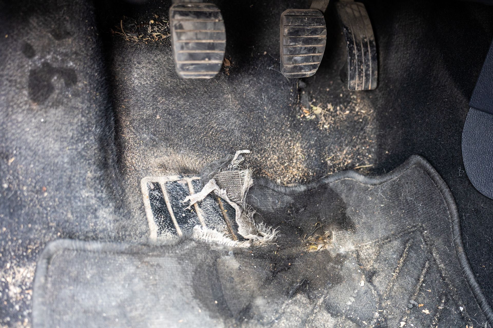 Close-up of dusty car foot pedals and floor mat with visible wear and debris Close-up of dusty car foot pedals and floor mat with visible wear and debris