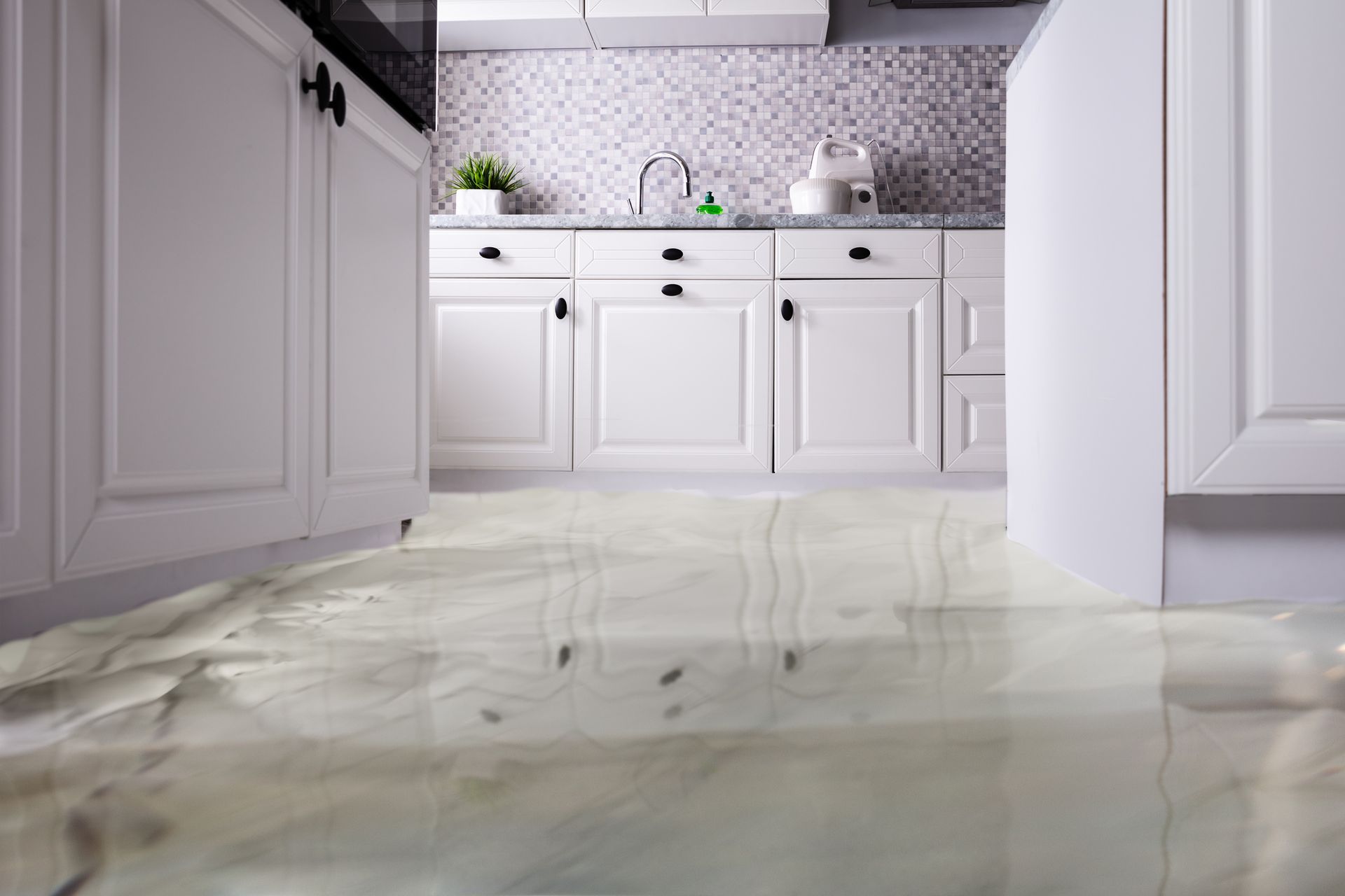 A kitchen with a flooded floor and white cabinets.