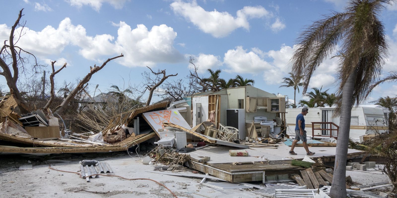 A man is walking through a hurricane damaged area.