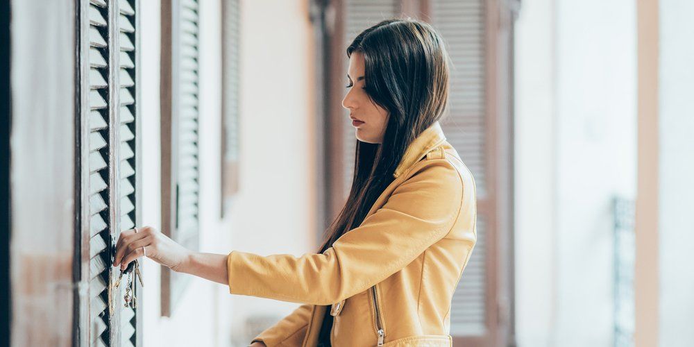 A woman in a yellow jacket is opening a window.