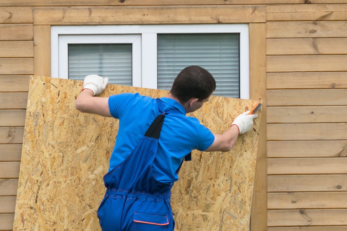 A man is holding a piece of plywood in front of a window.