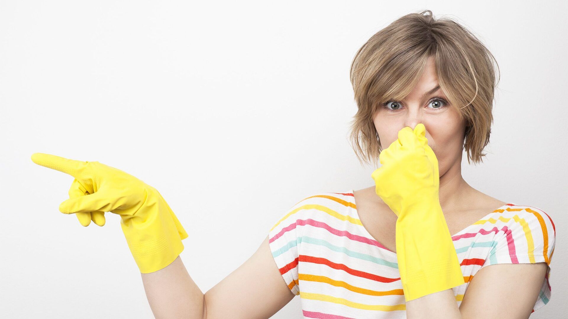 A woman wearing yellow gloves is covering her nose and pointing.