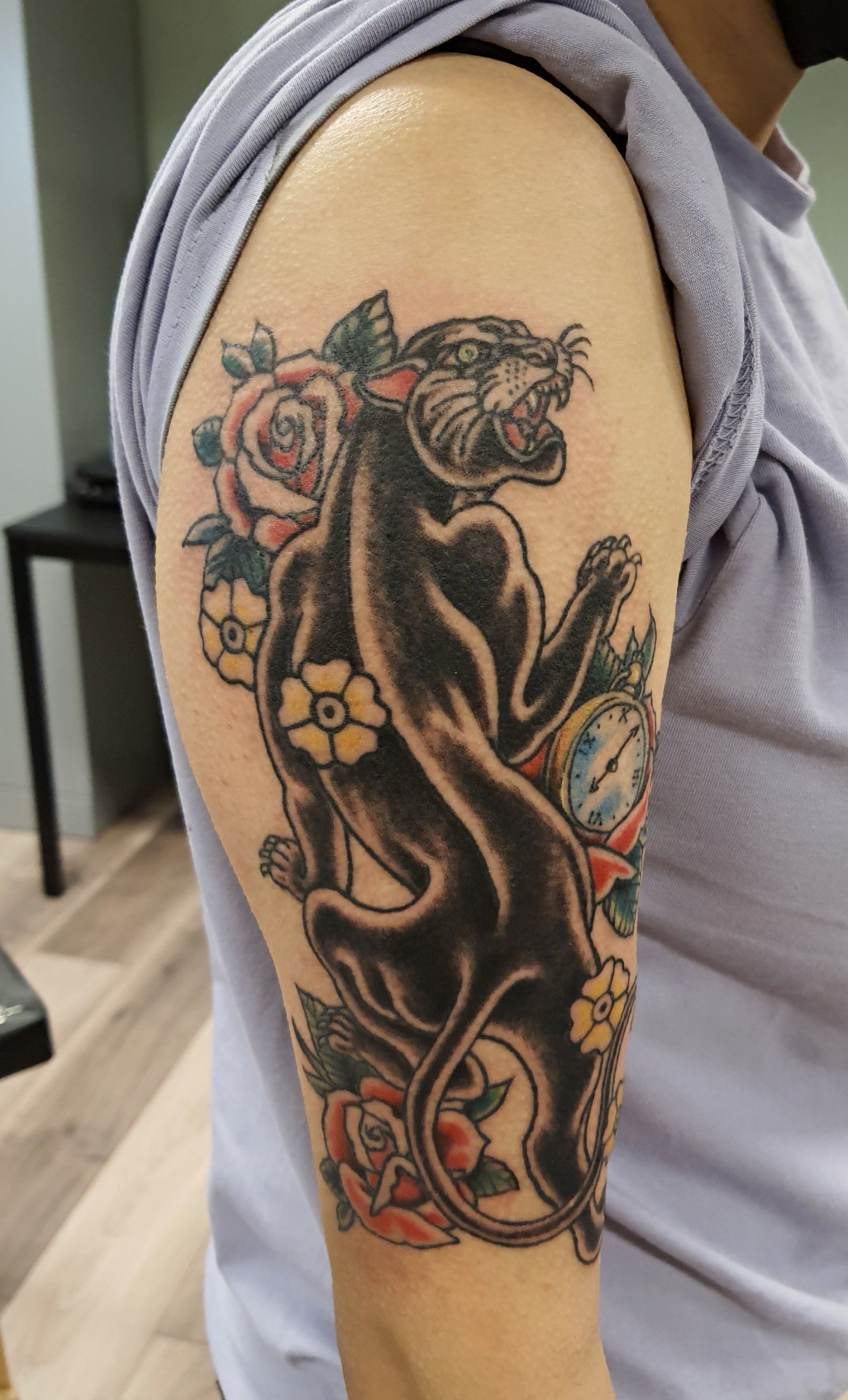 Gedetailleerde zwart-grijze bloementattoo op de bovenarm van een persoon, met rode en gele bloemaccenten.