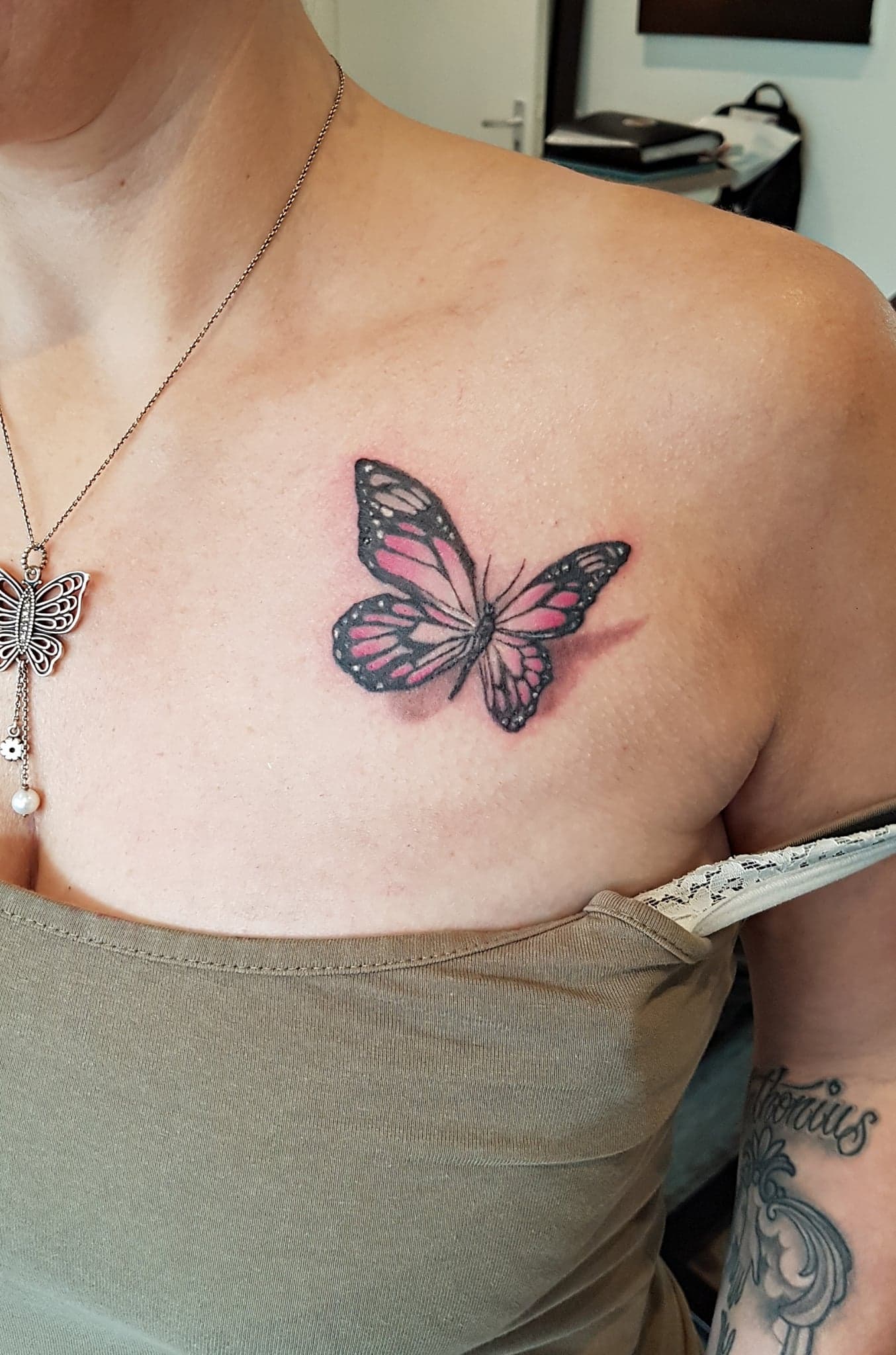 Roze en zwarte vlindertattoo op een schouder boven een strapless topje.
