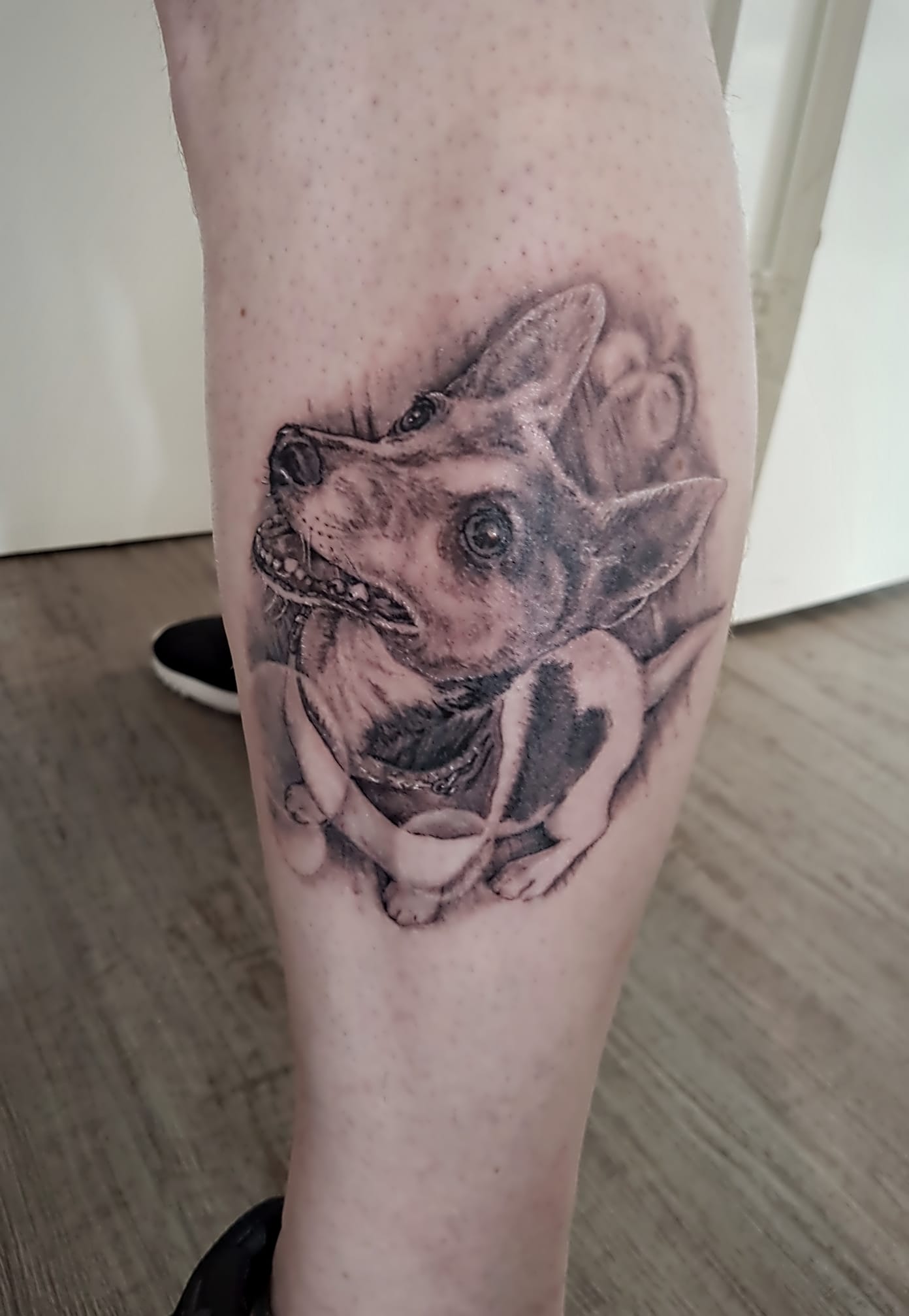 Zwart-grijze wolfstatoeage op een onderbeen, met gedetailleerde schaduwen en geometrische accenten.