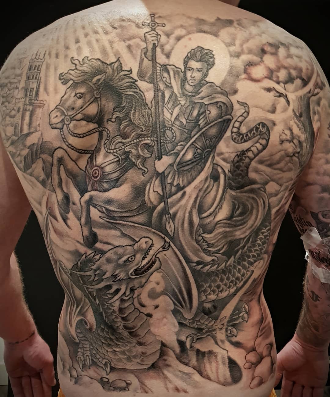 Tattoo op de rug van een ridder te paard in grijstinten, met dramatische wolken en een doodskopmotief.