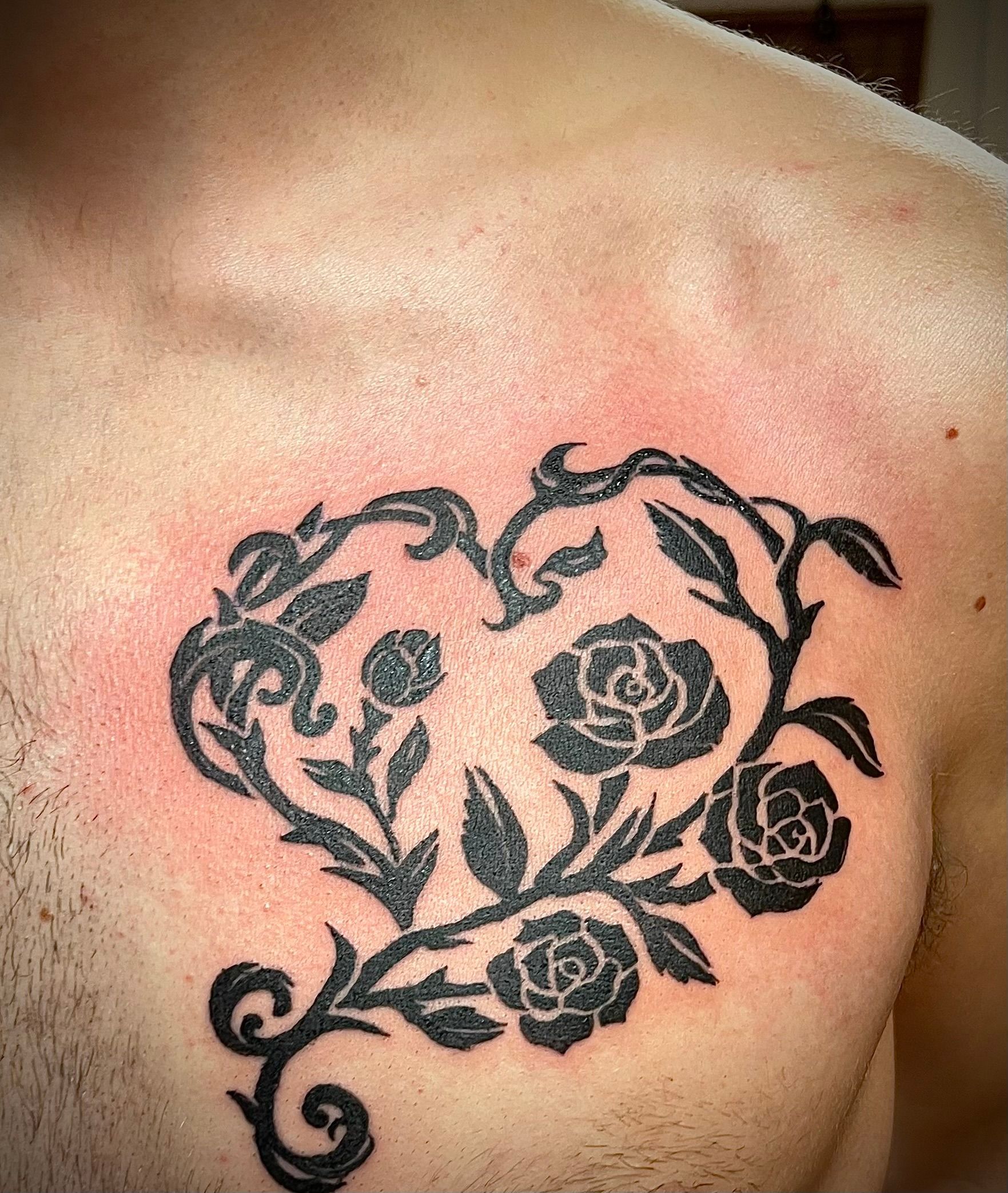 Zwarte bloemenranktattoo op een schouderblad tegen een lichte huid.