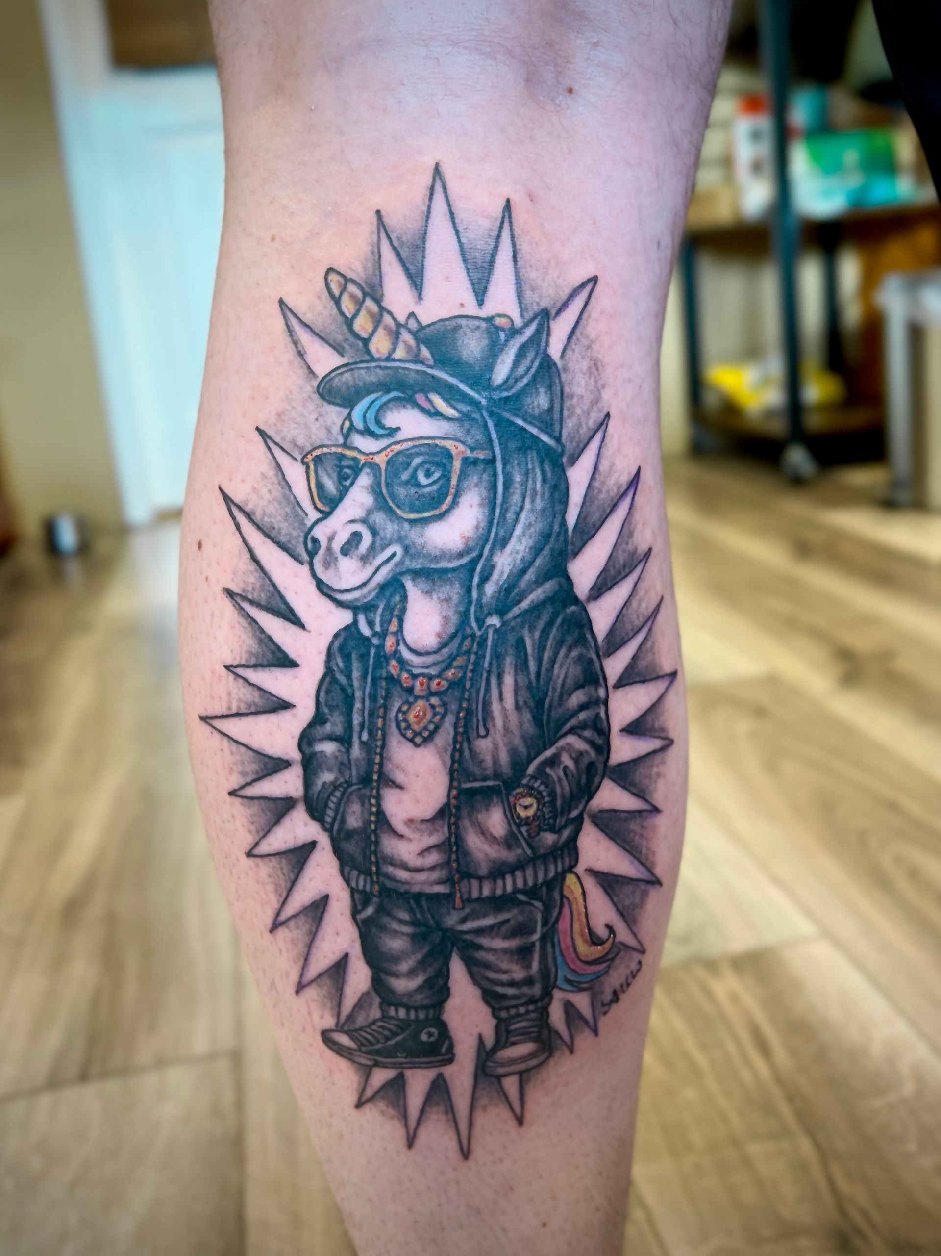 Zwart-grijze tatoeage van een gekroonde uil met een stekelige aureool op een onderarm.