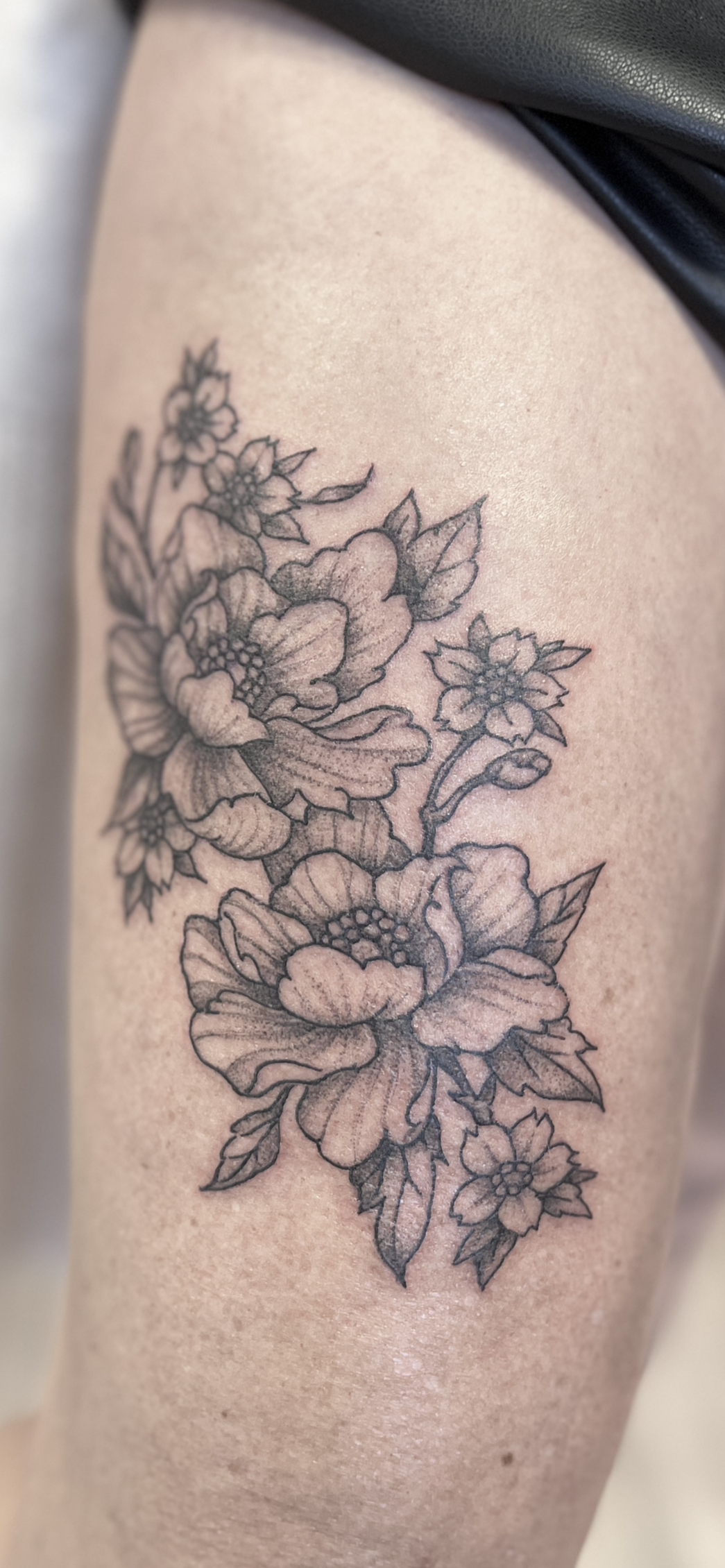 Zwarte bloementattoo op de huid van het bovenbeen/de heup.