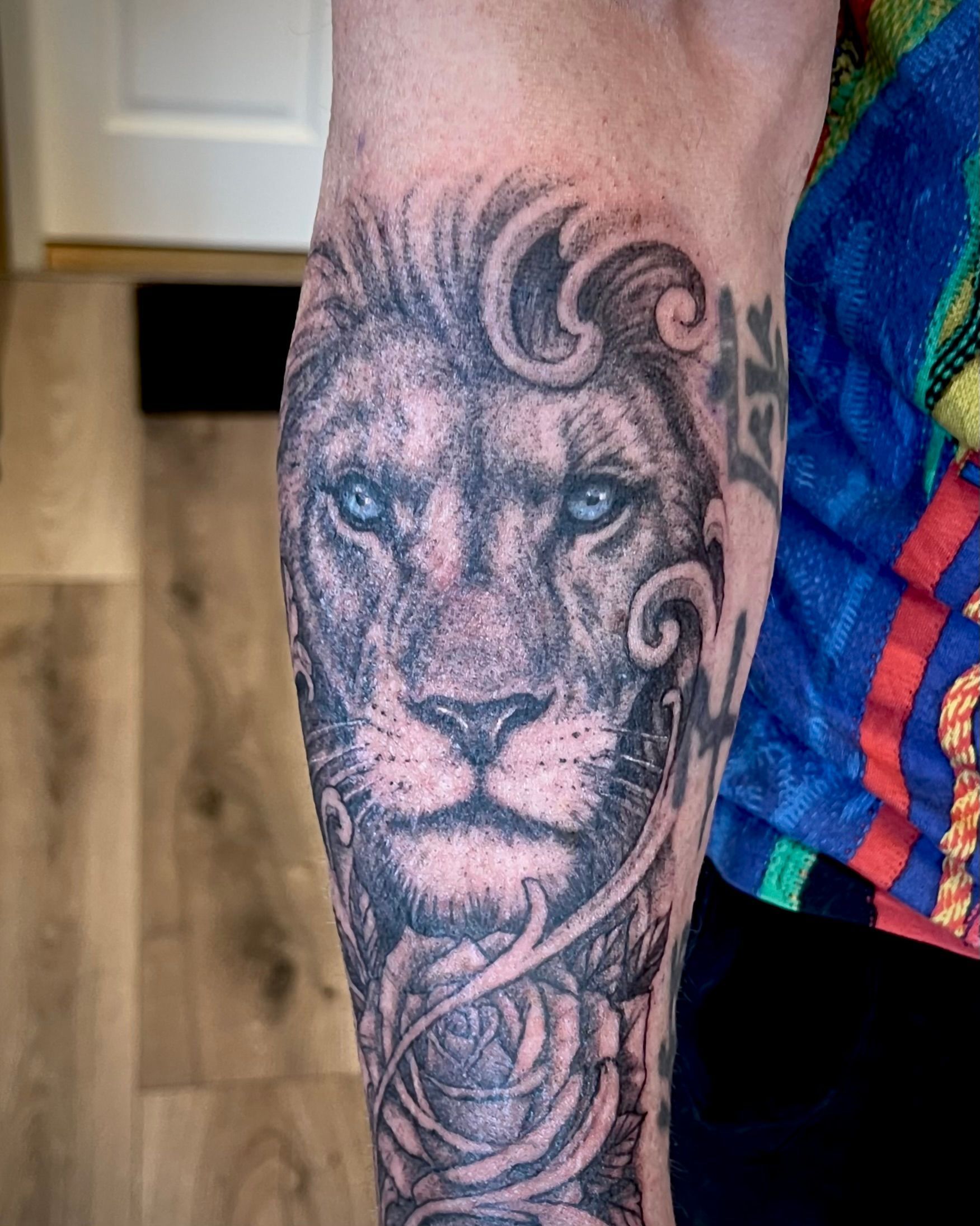Leeuwentattoo op een onderarm met sierlijke, wervelende zwart-grijze details.