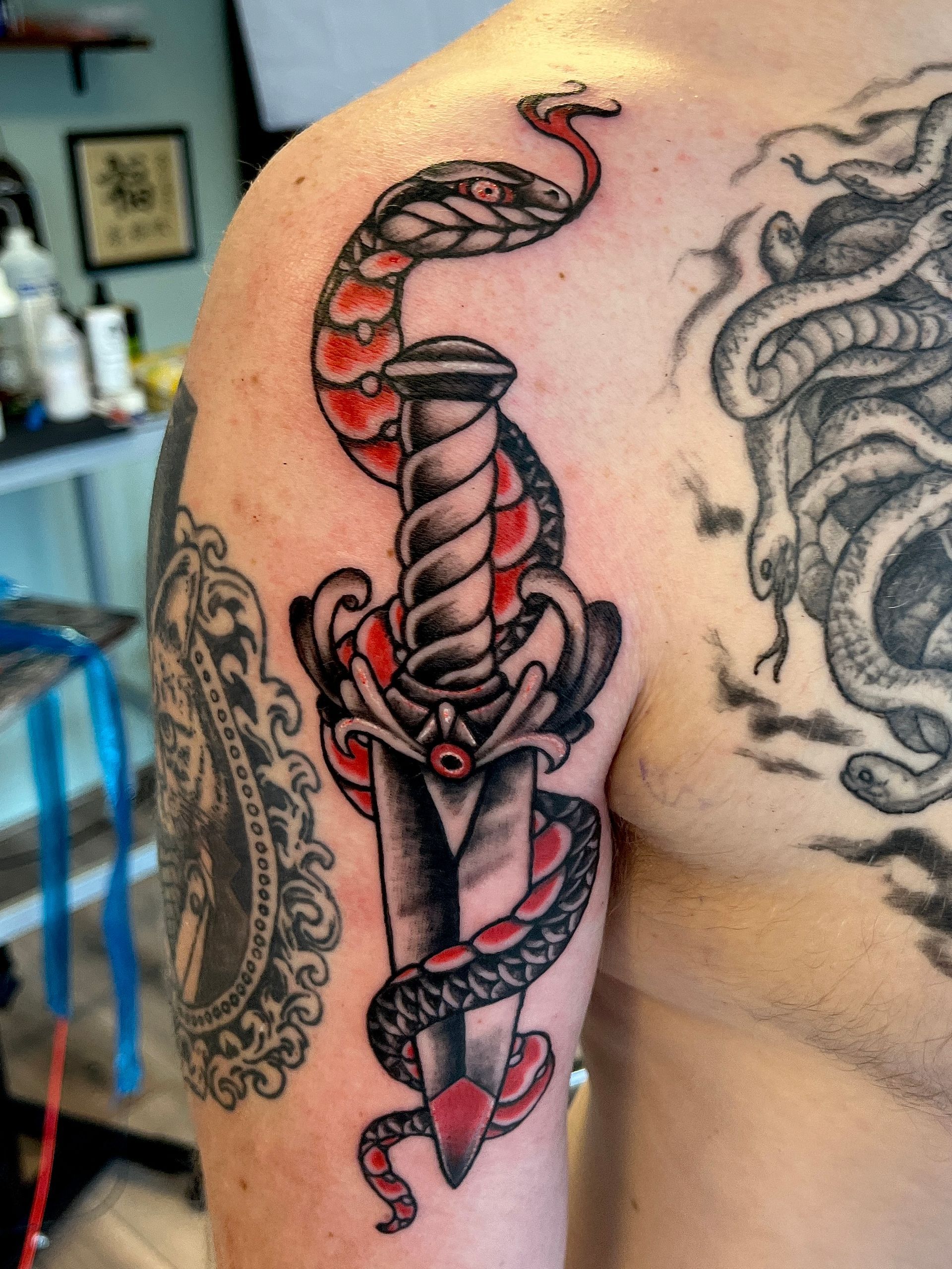 Getatoeëerde bovenarm met een rood-zwarte dolk, verstrengeld met een slang en accenten van een schedel.