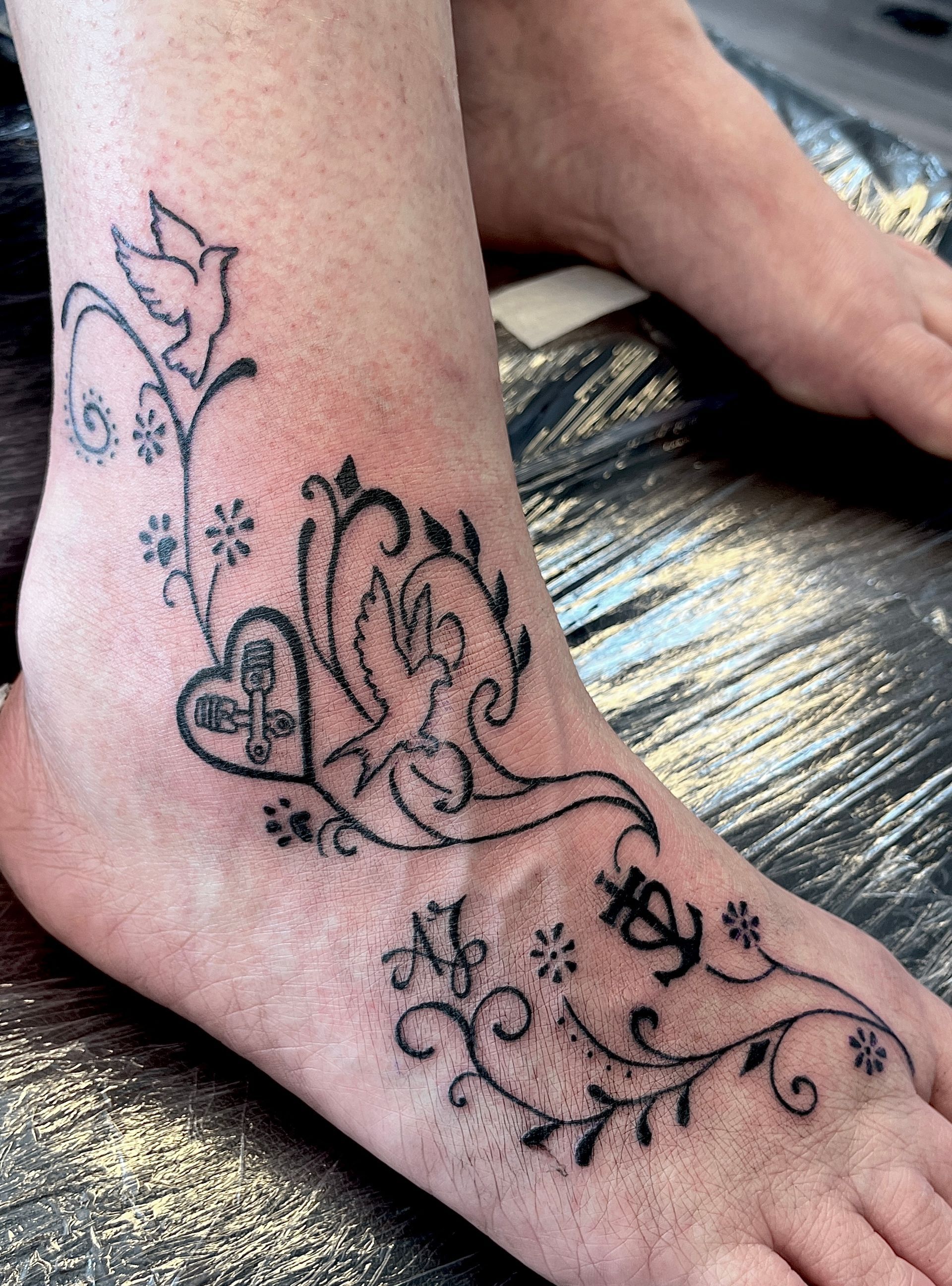 Armtattoo met zwarte bloemen- en hartmotieven op de onderarm.