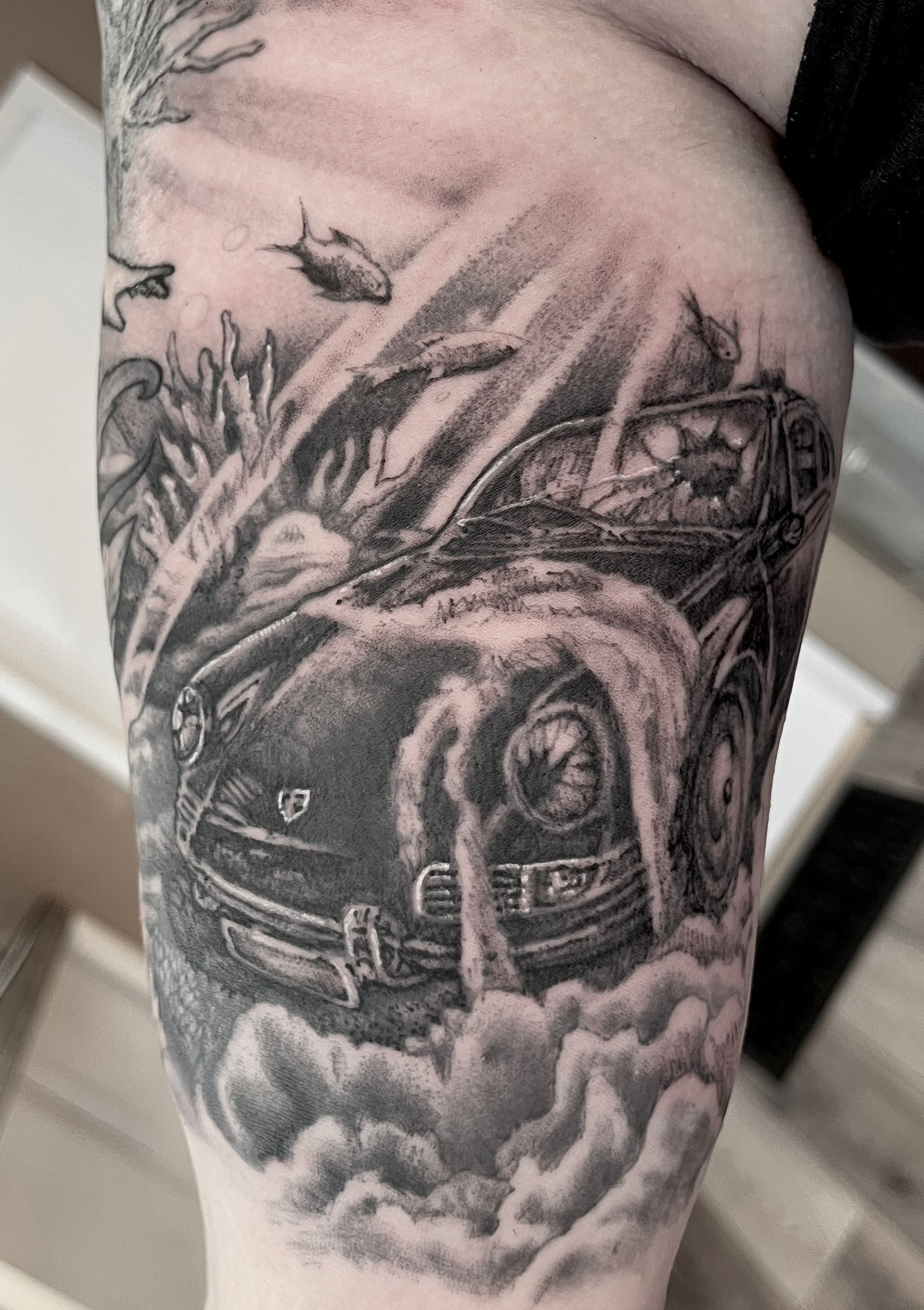Zwart-grijze tatoeage van een muscle car omgeven door rook op een onderarm.