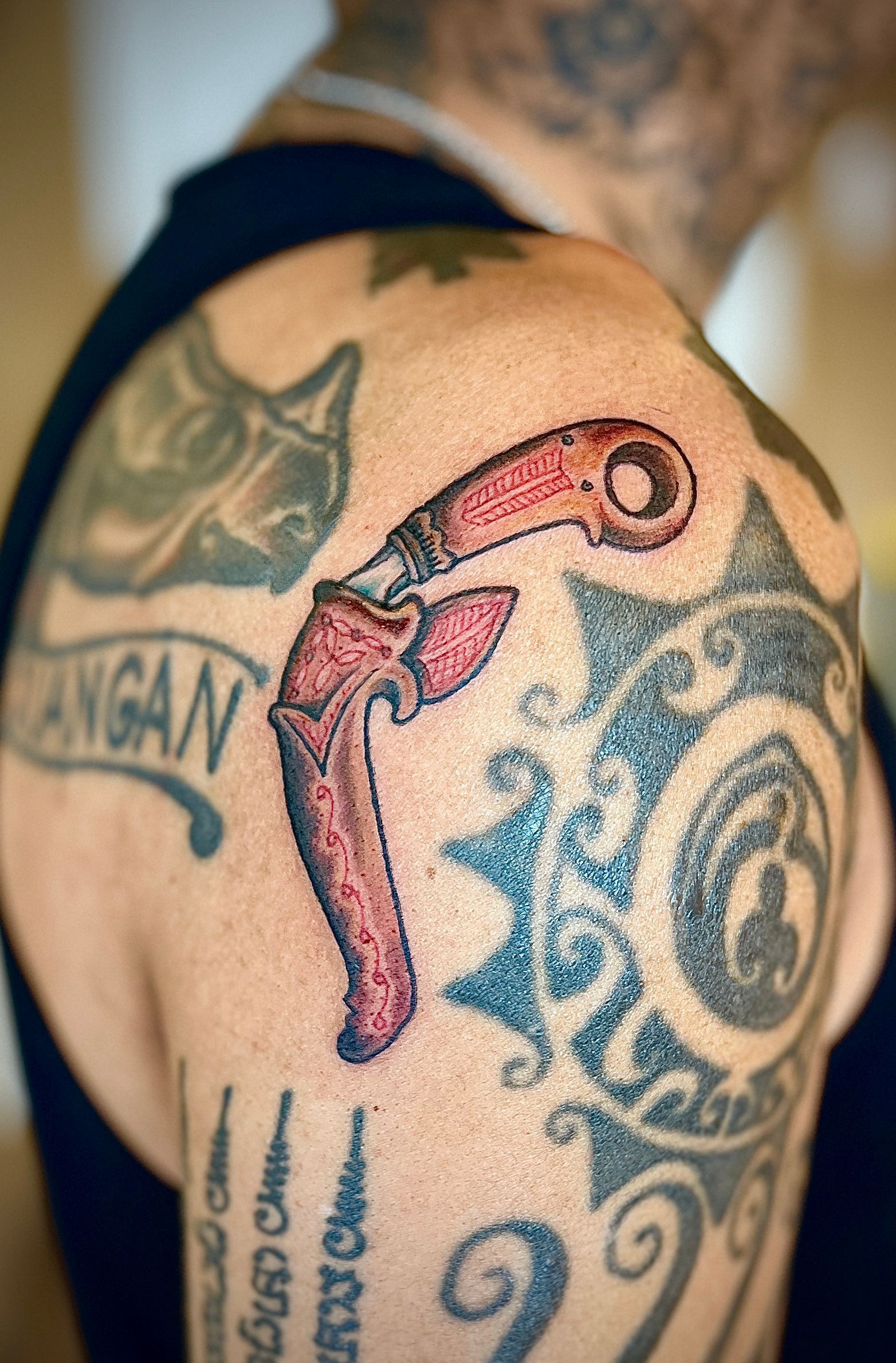 Close-up van een tatoeage op het been met een roze hamer en blauwe krullen op de huid.
