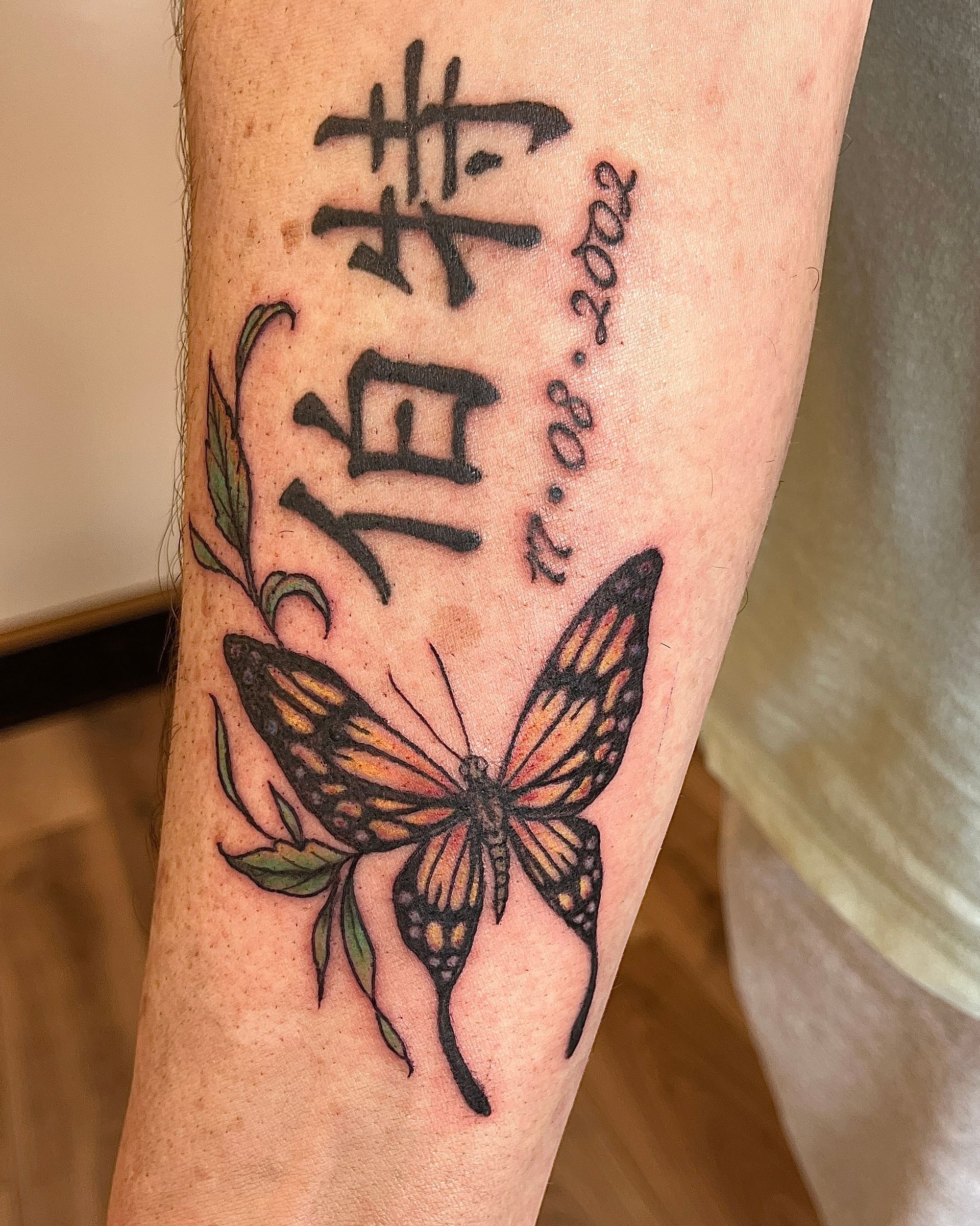Tattoo op de onderarm van een vlinder met Chinese karakters in zwarte inkt.