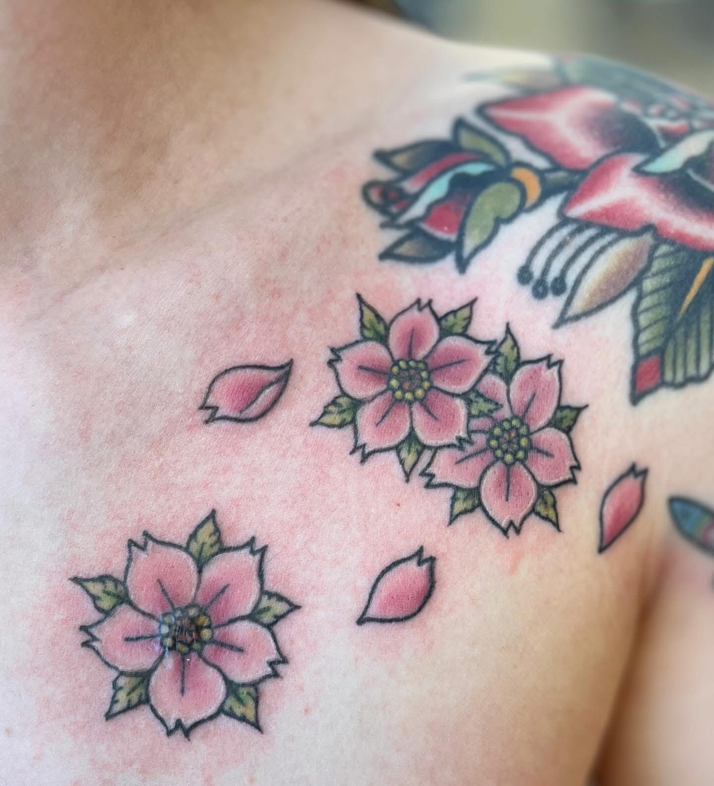 Close-up van een schoudertattoo met roze bloemen en groene bladeren op de huid.