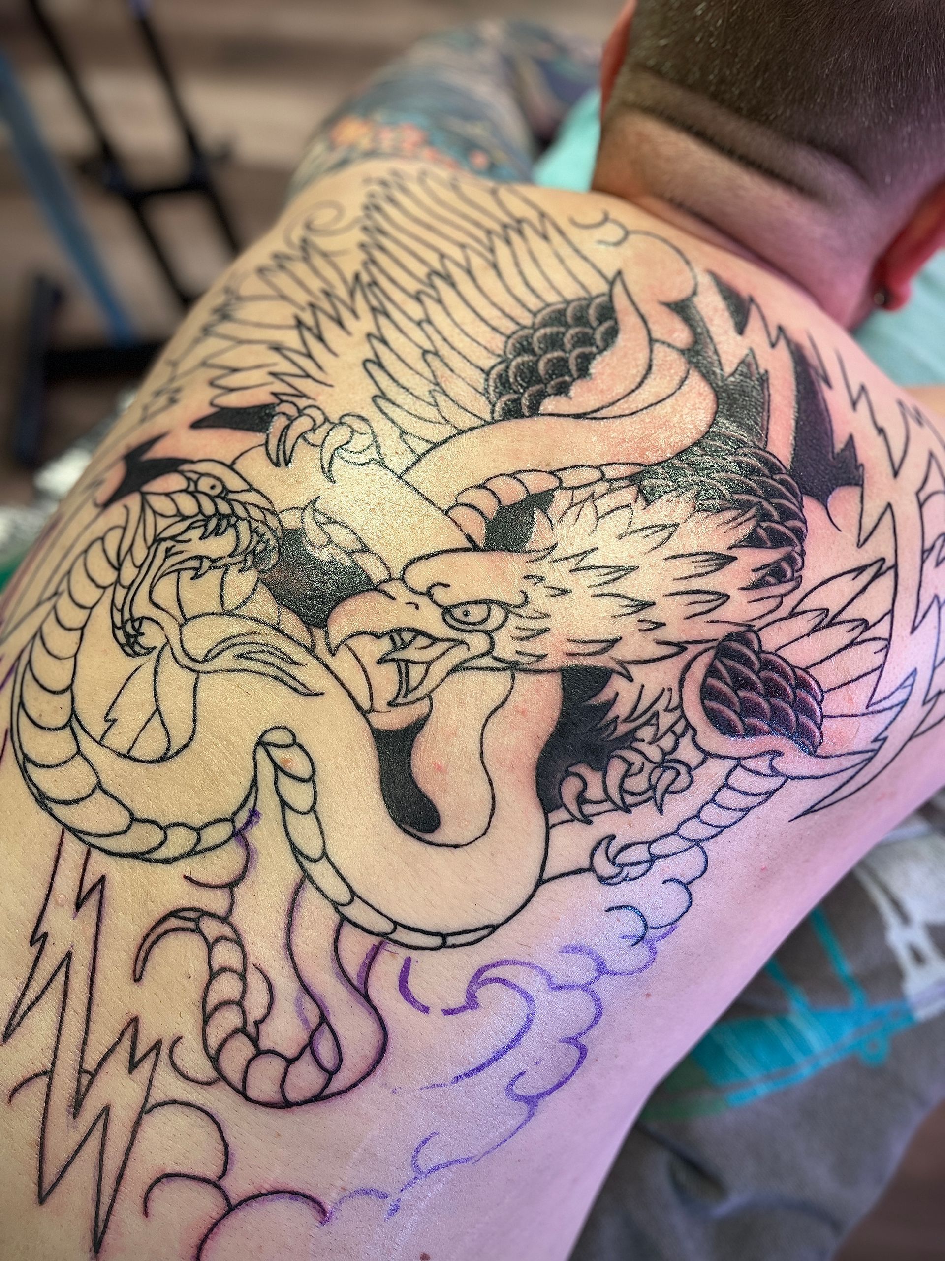 Een grote zwart-witte drakentattoo op de bovenrug van een persoon, in uitvoering met zichtbare sjabloonlijnen.