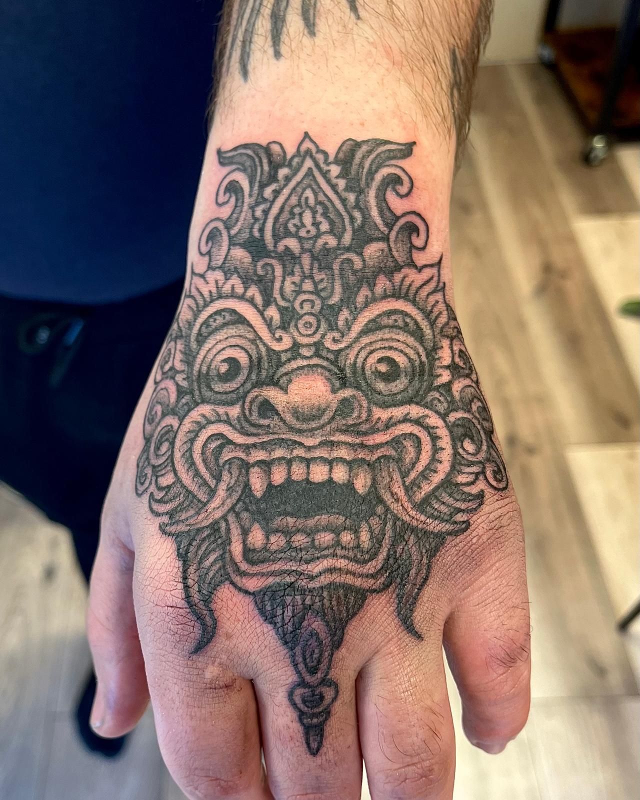 De achterkant van een hand met een gedetailleerde zwart-grijze tatoeage van een woest gezicht.