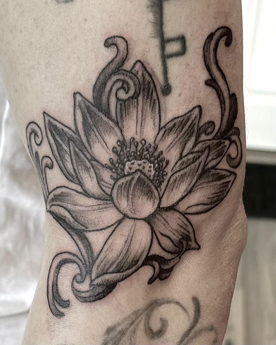 Zwarte lijntekening van een lotusbloemtattoo op de pols met bloem- en kruldetails.
