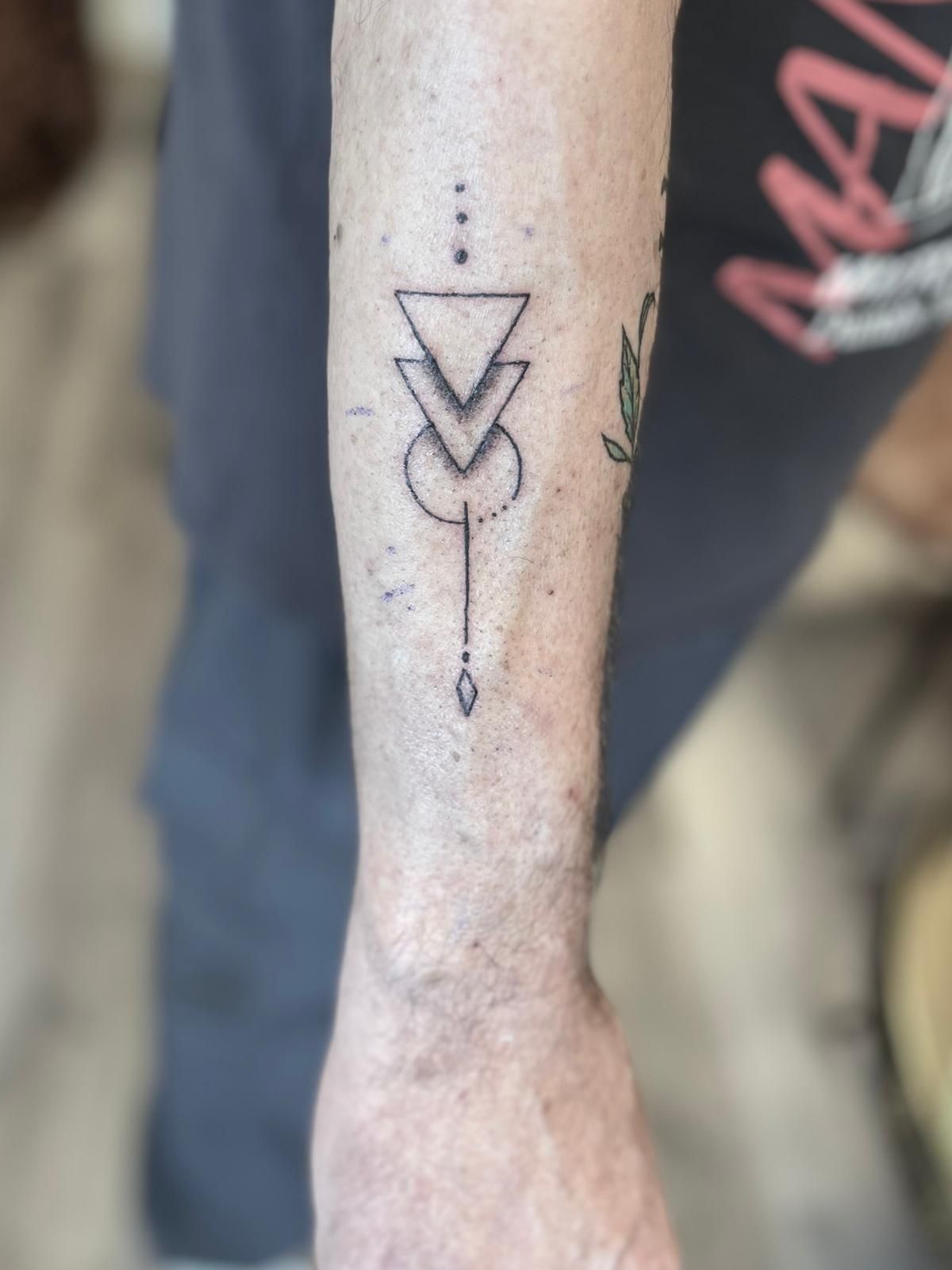 Onderbeen met een zwarte geometrische tatoeage op de kuit tegen een wazige achtergrond.